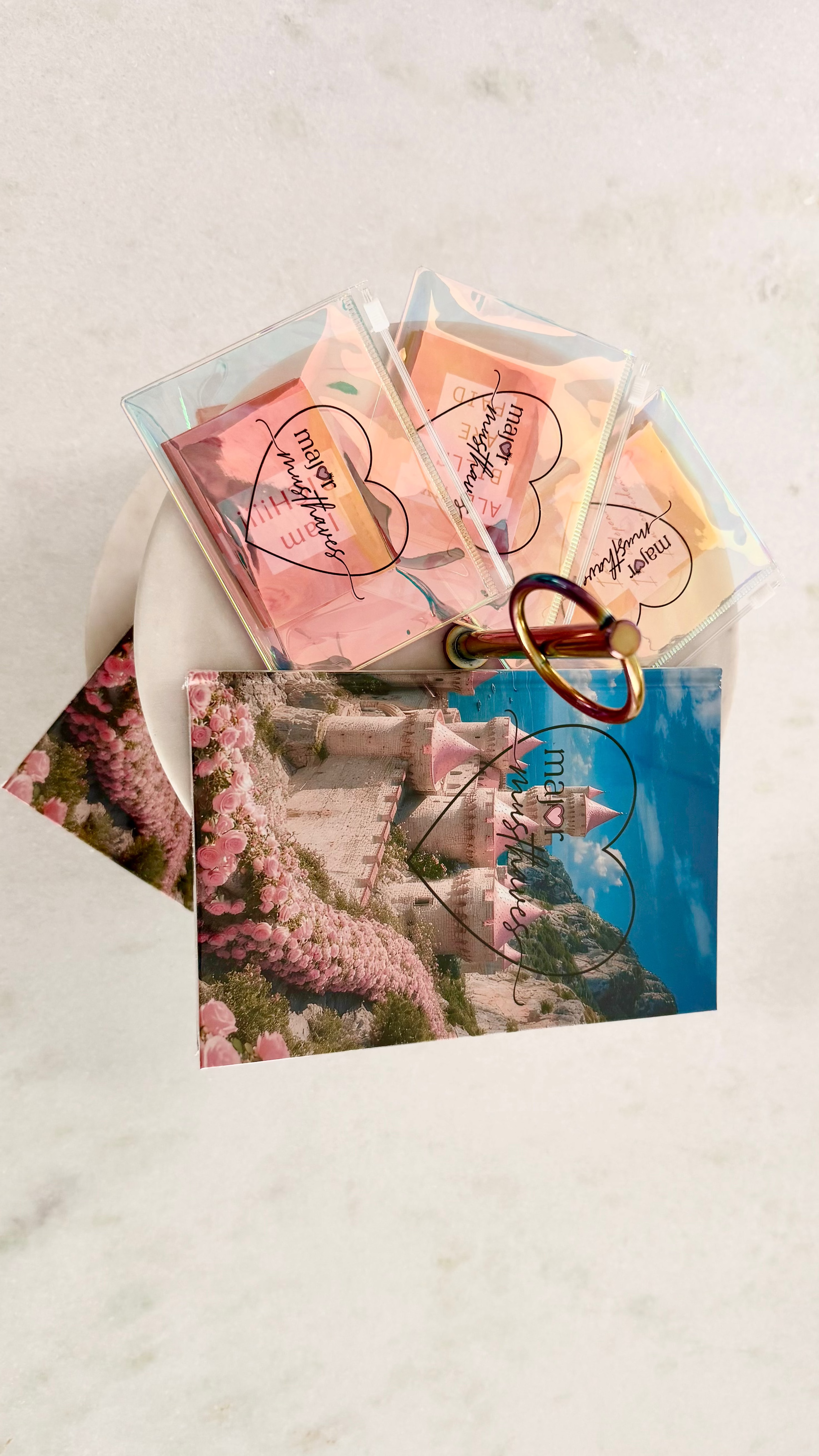 A set of wax melts in clear plastic bags with a gold heart-shaped ring holder, displayed next to a printed card featuring a castle and pink flowers on a white marble background.